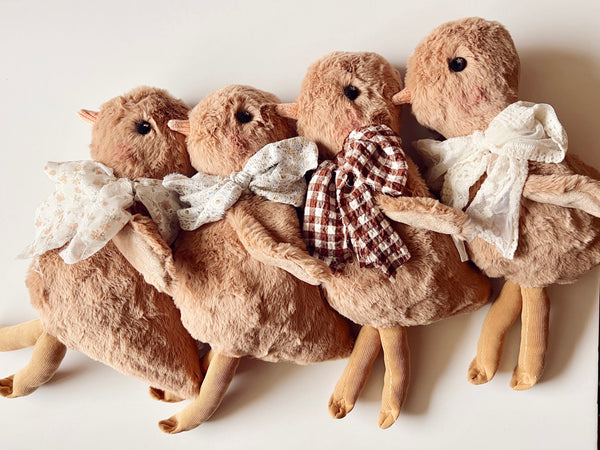 Four plush toys resembling ducks with plaid and lace accessories on a white background