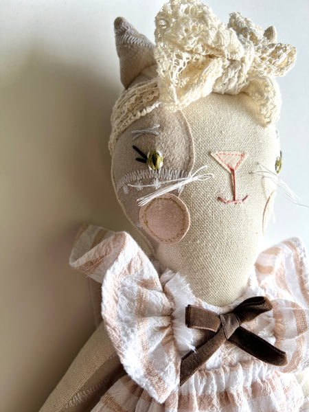 Textile cat doll with lace details on a neutral background