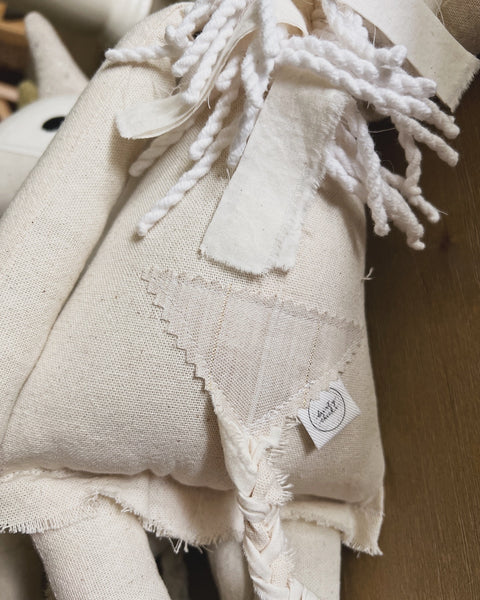 Close-up of a unicorn doll/s tail with braid and a visible brand tag on a wooden surface.