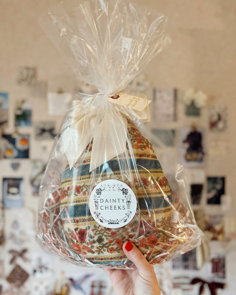 Decorative egg cushion wrapped in cellophane with a visible brand label, held against a wall with photos.