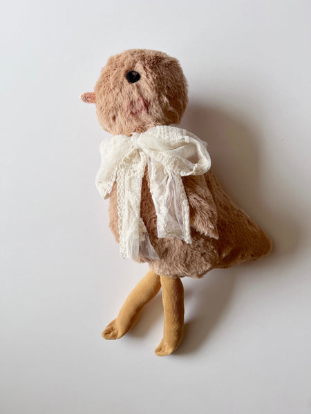 Stuffed chick wearing a white lace tie on a plain background