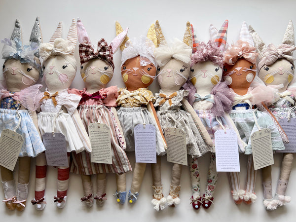 Row of handmade dolls with various outfits and accessories on a white background