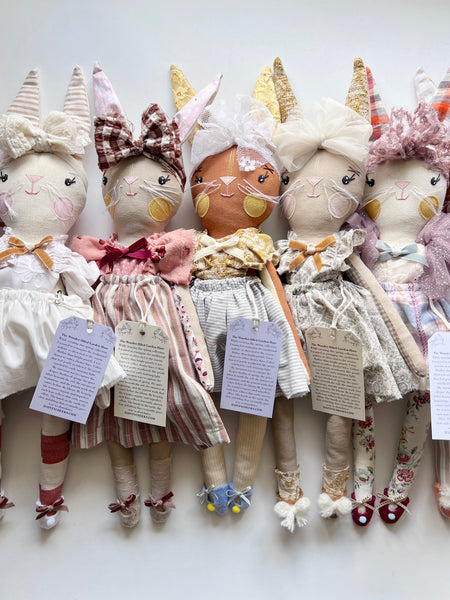 Row of handmade hare dolls with various outfits and accessories on a white background