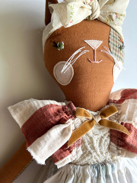 Cat doll with a headband and dress on a plain background