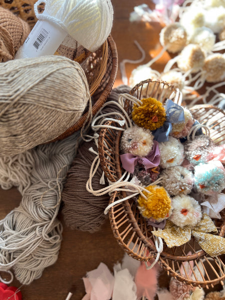 Balls of yarn and chick pom charms in a basket on a wooden surface