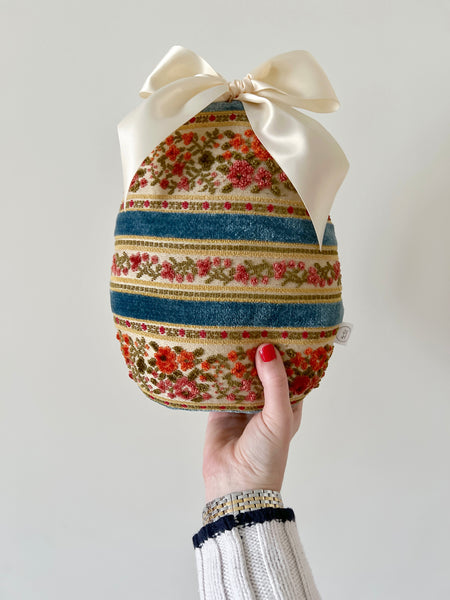 Decorative Easter egg with floral pattern and striped design, held by a hand against a plain background